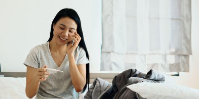 Young woman looking happily at her pregnancy test whilst on the phone