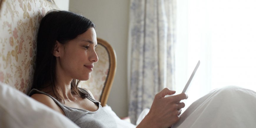 Woman lying down in bed with tablet